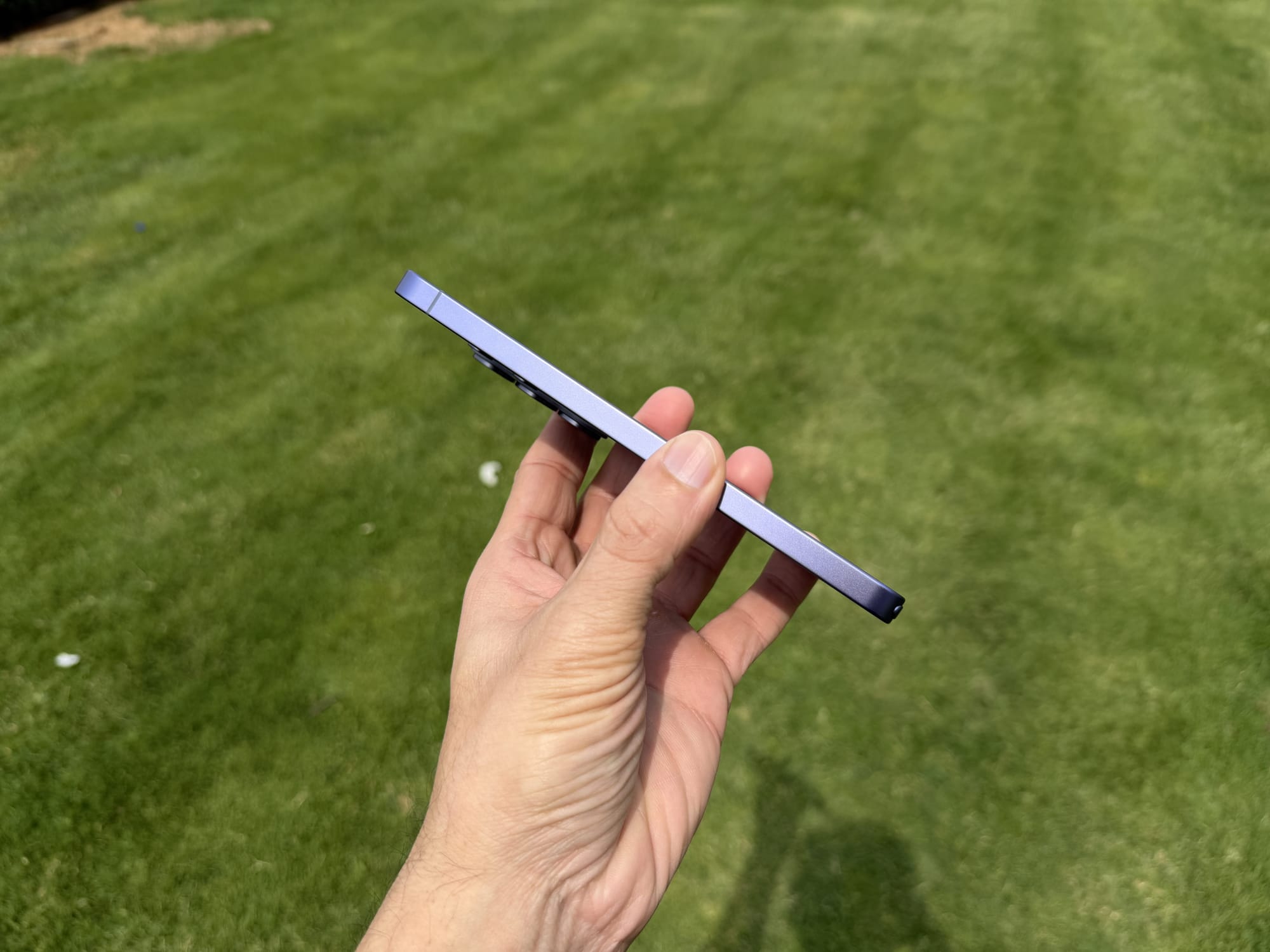 User holding the Samsung S26 Ultra at an angle, highlighting its thin profile against a grassy background.