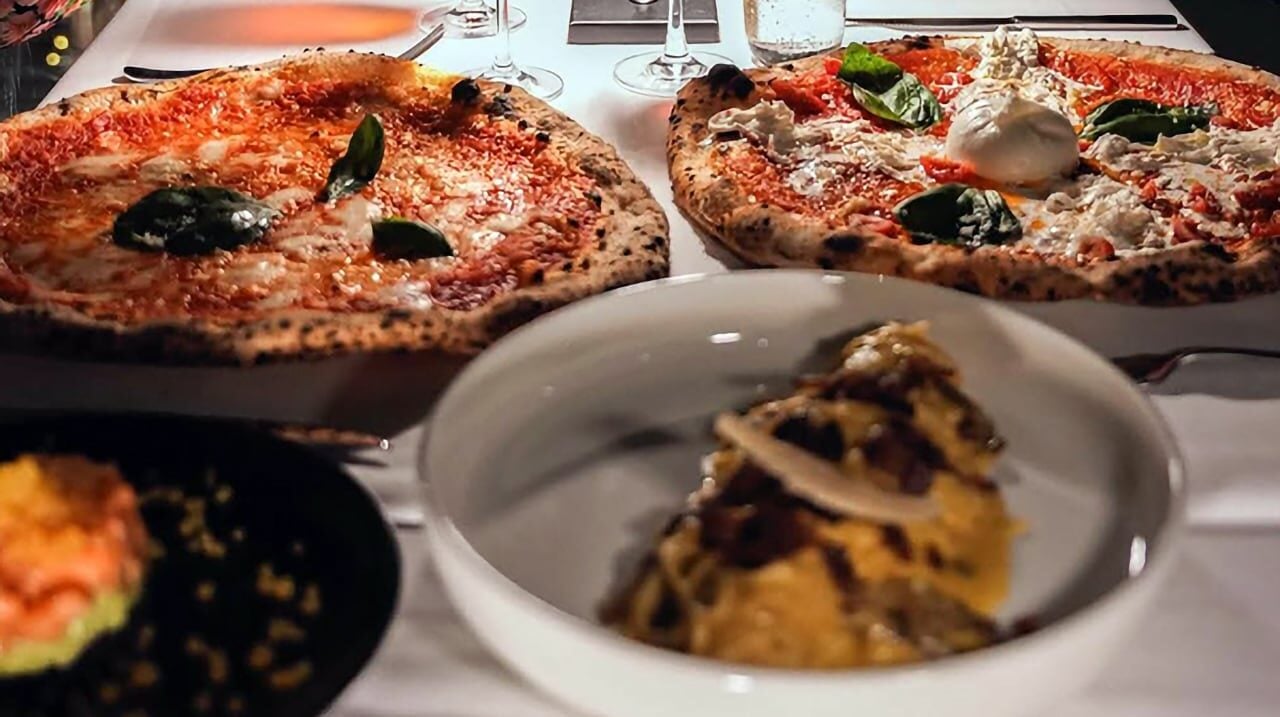 Pizza, burrata and pasta on a white-clothed table at a Dubai restaurant