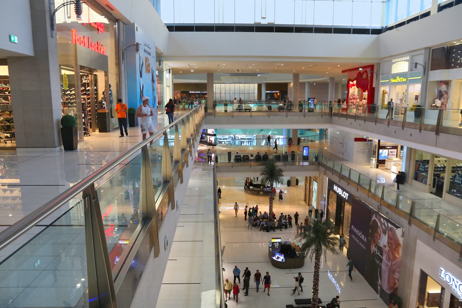 Sunlit interior of Dubai Mall with palm trees and shoppers on the upper walkways