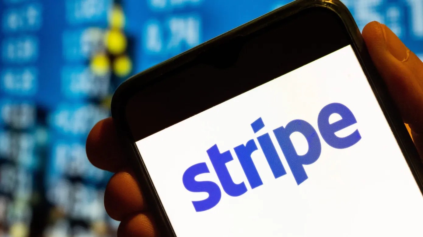 A hand holding a smartphone displaying the Stripe logo against a blurred blue background