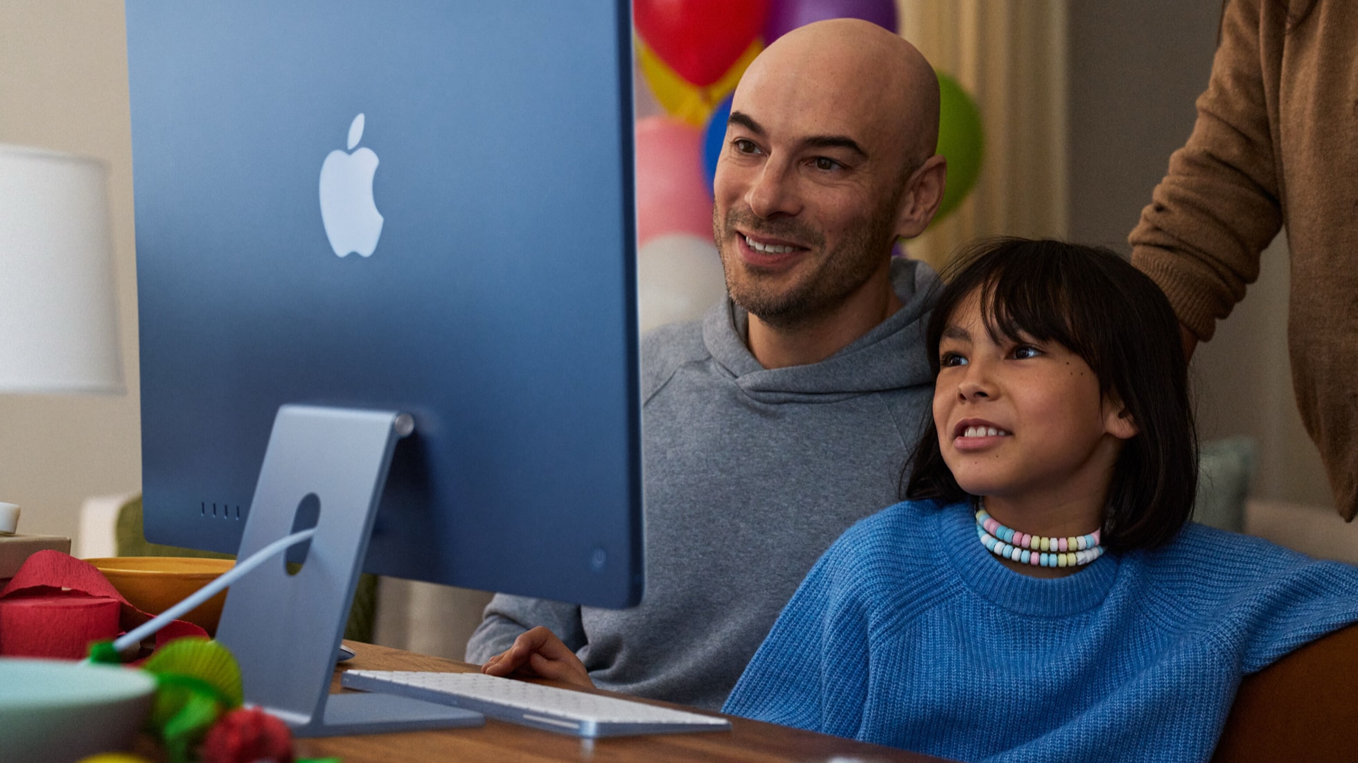 A father and daughter sit together at an iMac at home