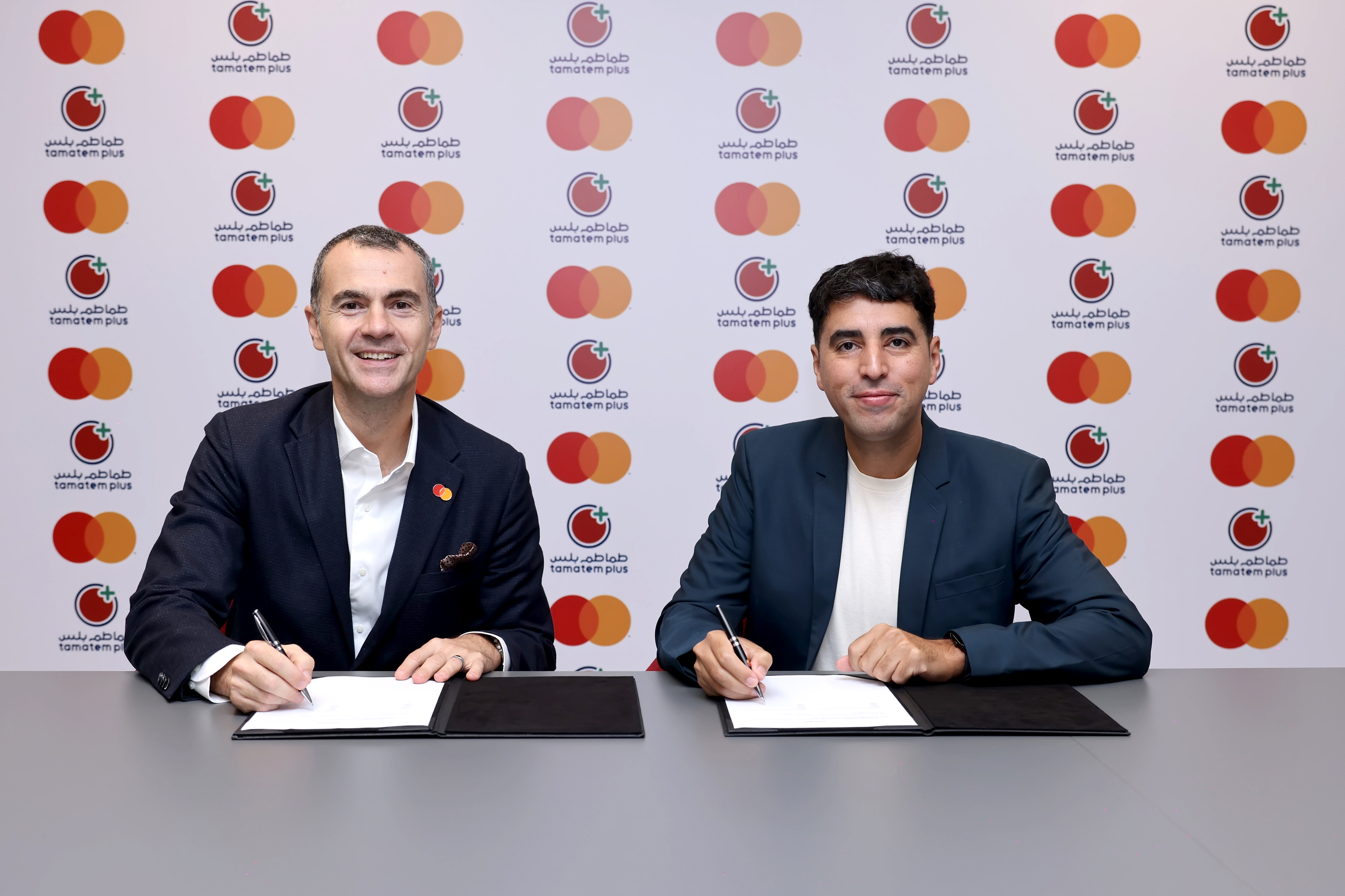 Mastercard and Tamatem Plus executives signing a partnership agreement in front of a branded backdrop